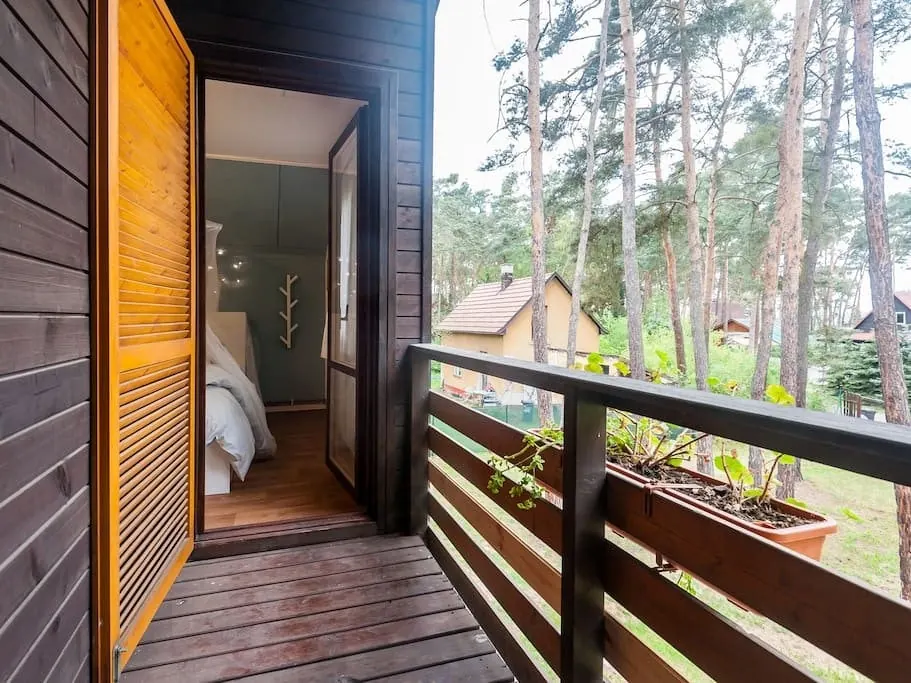 Balkon s dřevěným zábradlím, za ním borovice