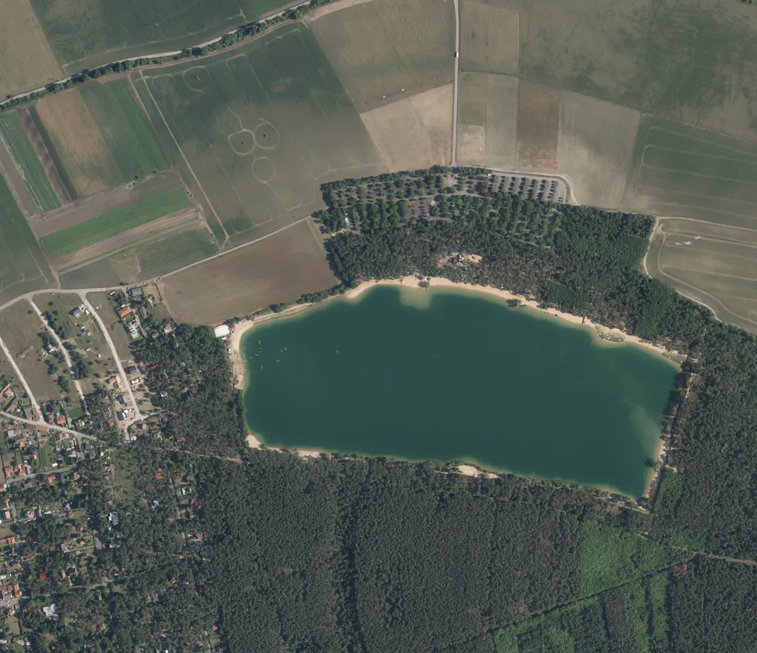 Letecký snímek z roku 2025: jezero Lhota mezi borovým lesem a domy Lhoty
