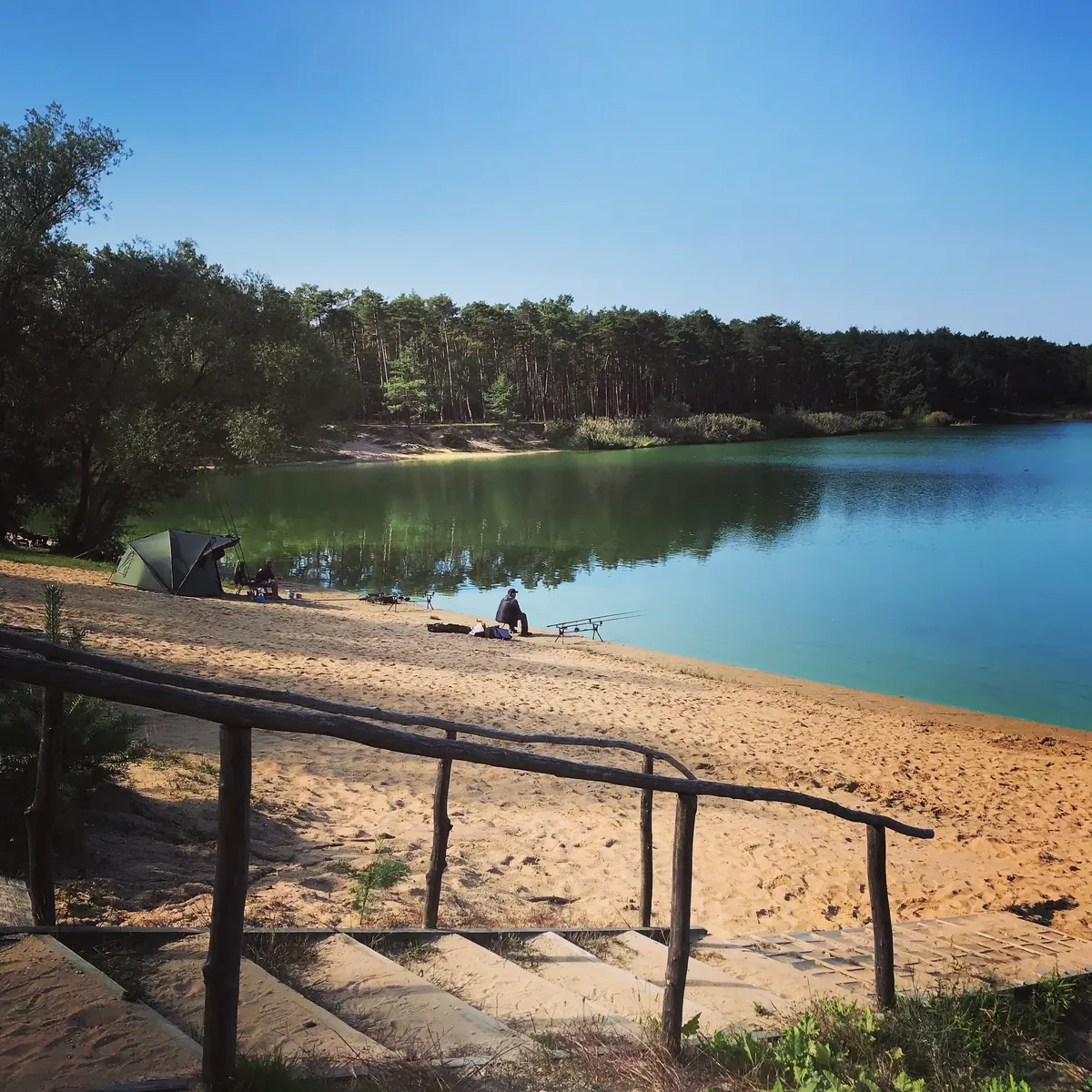 Dřevěné schody na písečnou pláž, za nimi jezero a borový les