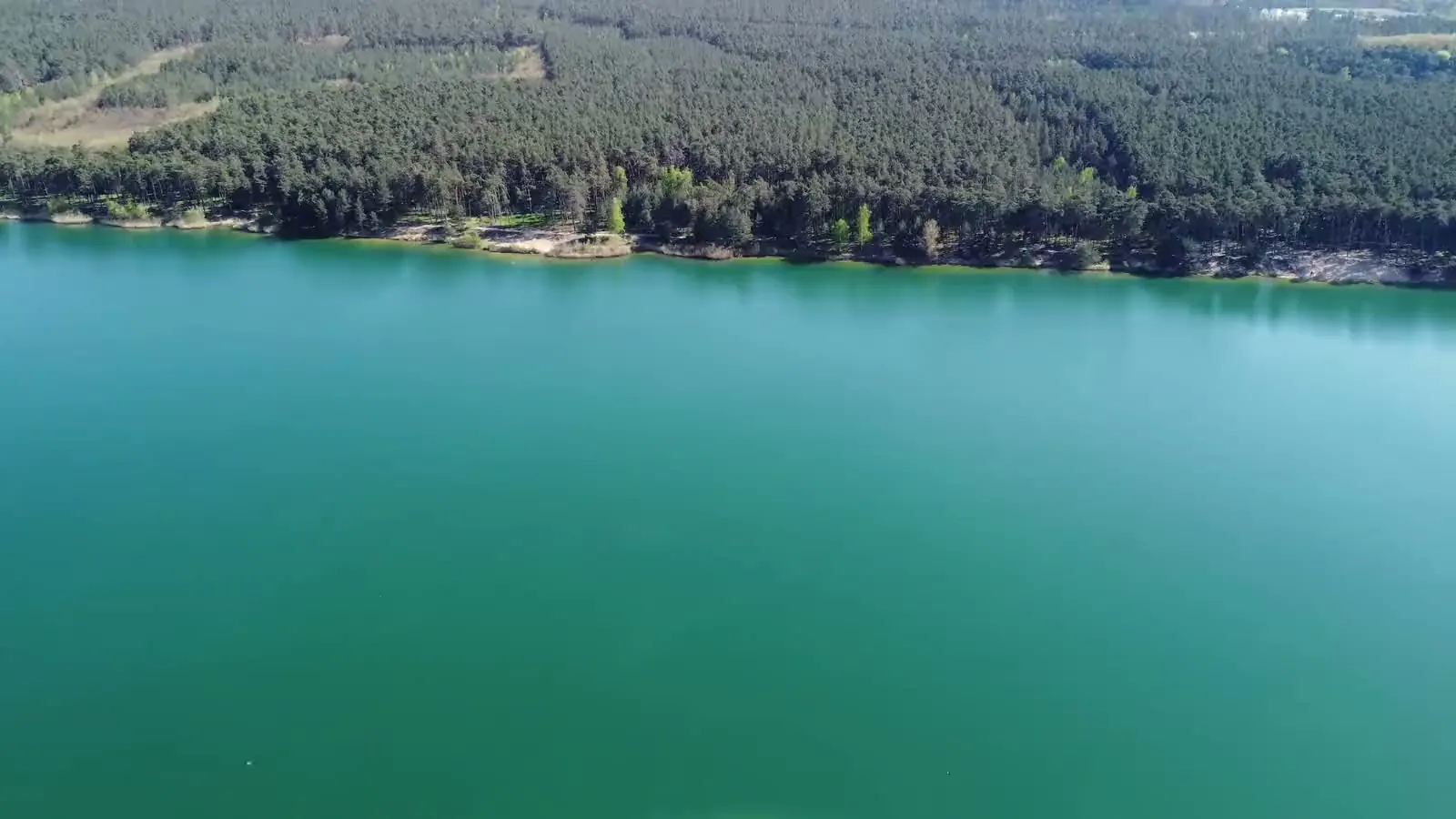 Průzračná voda nad písečnou mělčinou u břehu, záběr z dronu