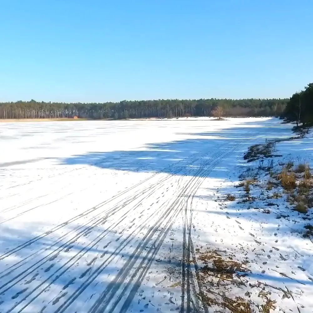 Zamrzlé jezero pod sněhem s dlouhými stíny borovic, záběr z dronu